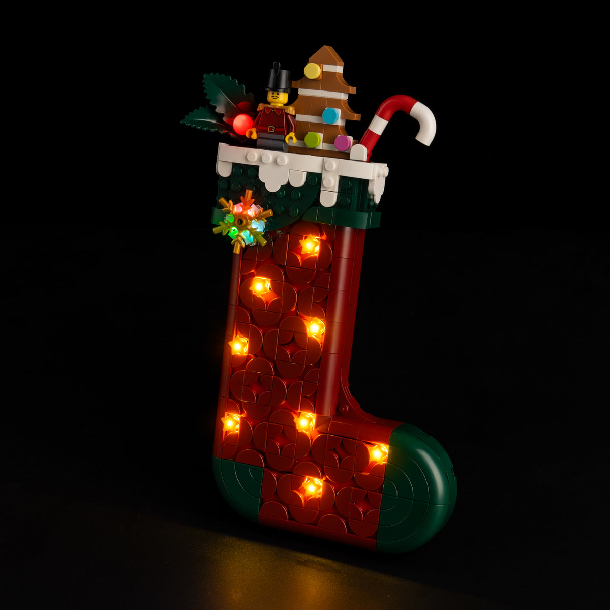 Real Shopify front-quarter photograph of LEGO® Christmas Stocking 40958 with its eight warm stars, red berry and multicolor snowflake lit.