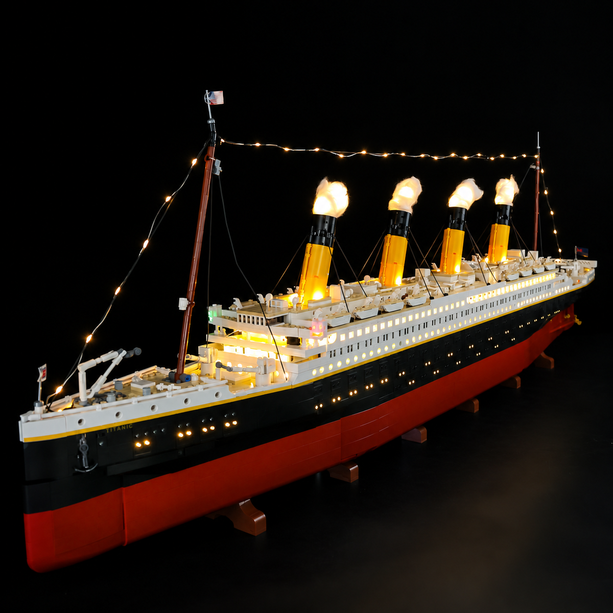 LEGO Titanic 10294 with warm LED lights along the hull, illuminated funnel tops and rigging, viewed from the bow.